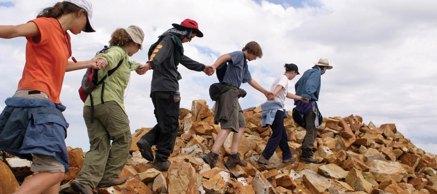 Students join hands to walk across rocks.