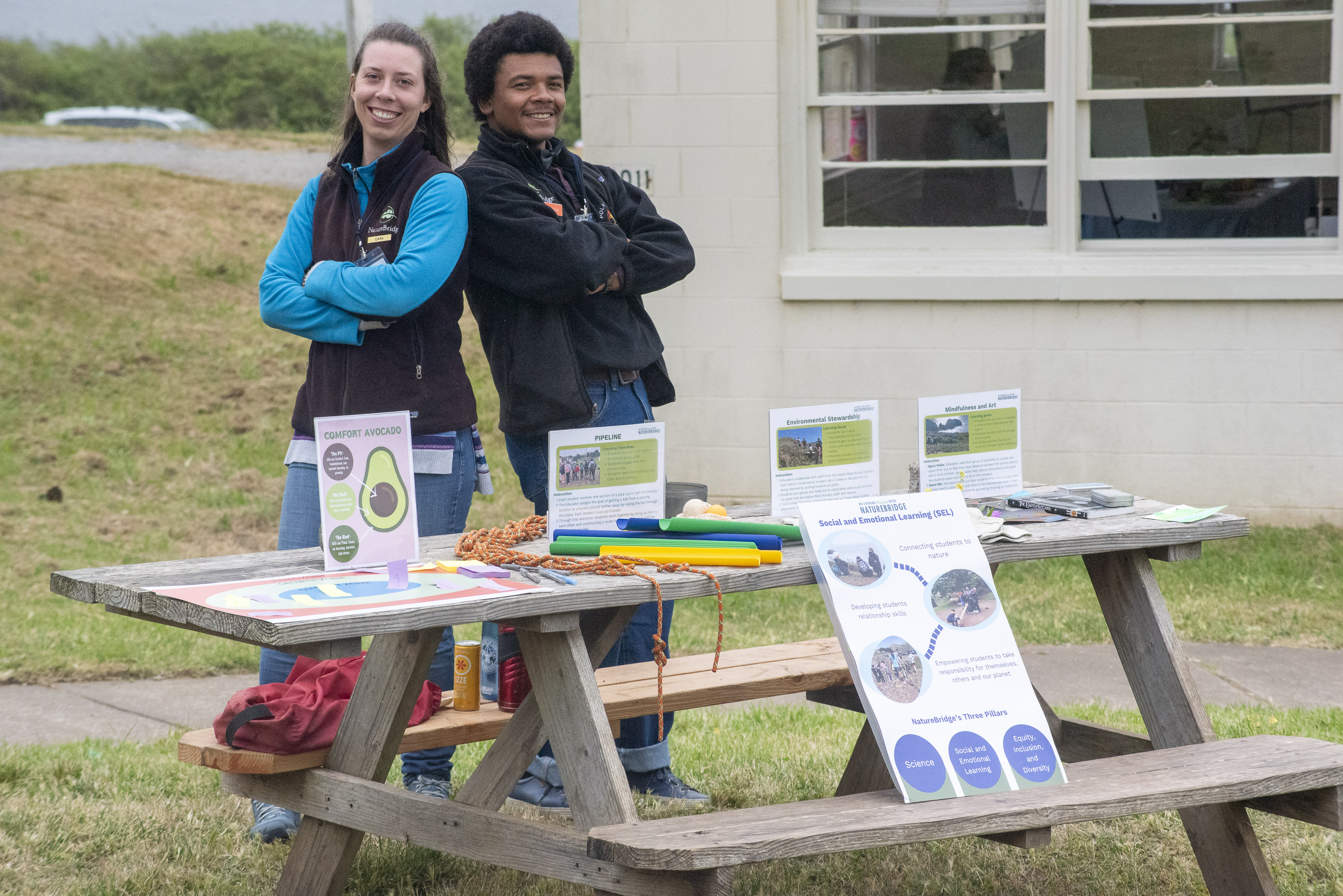 Two NatureBridge educators standing behind a wooden picnic table covered with learning materials
