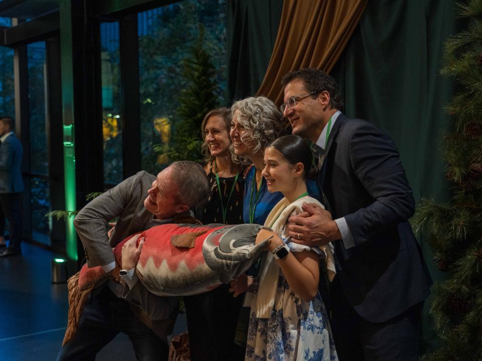 A group of adults and one child posing for a group photo while holding a large plush toy shaped like a salmon