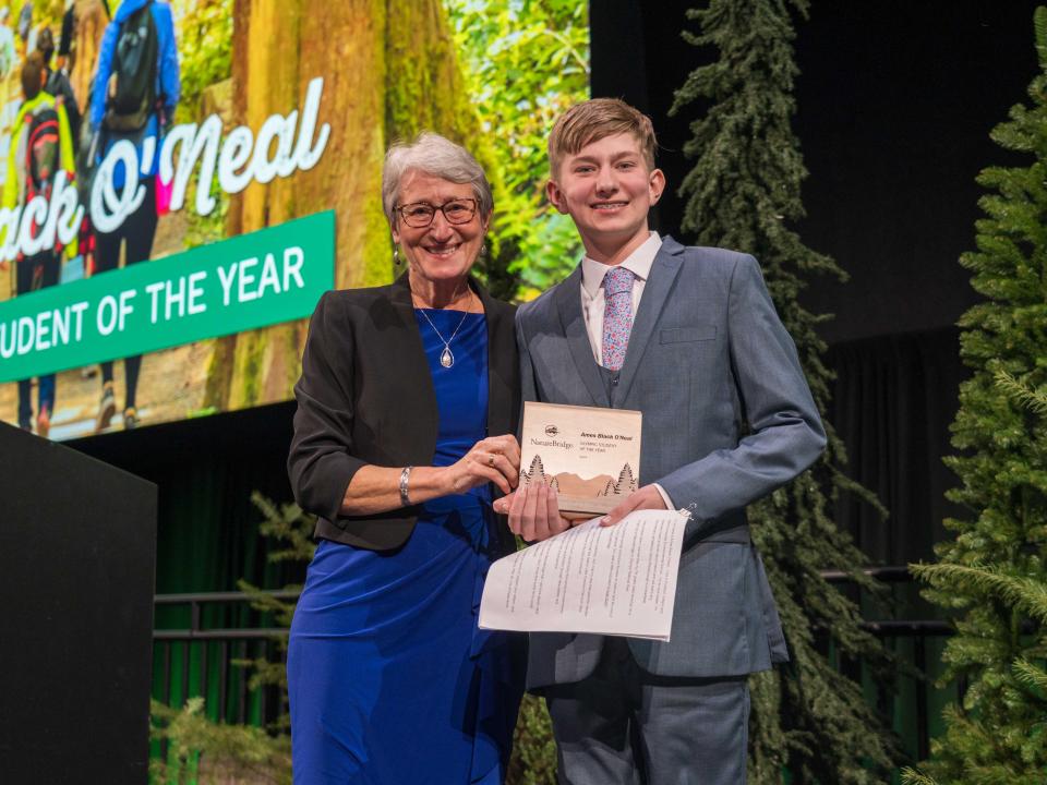 Sally Jewell and Ames Black O'Neal posing together onstage with his Olympic Student of the Year award