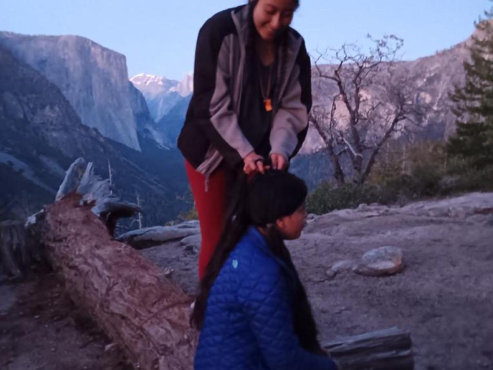 New Village Academy WildLink participant braiding her friends hair with Yosemite valley in the background. 