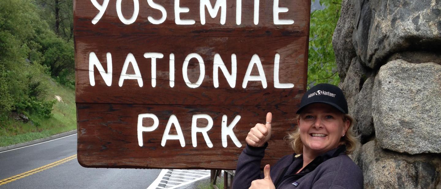 yosemite national park entrance sign with woman in hat smiling 